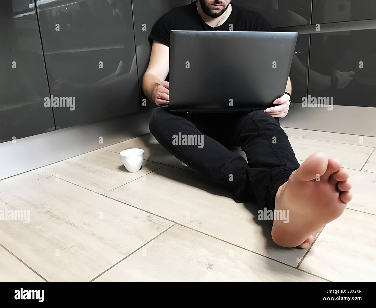 Young man using laptop and drinking coffee at home - Smartphone Captured Stock Image