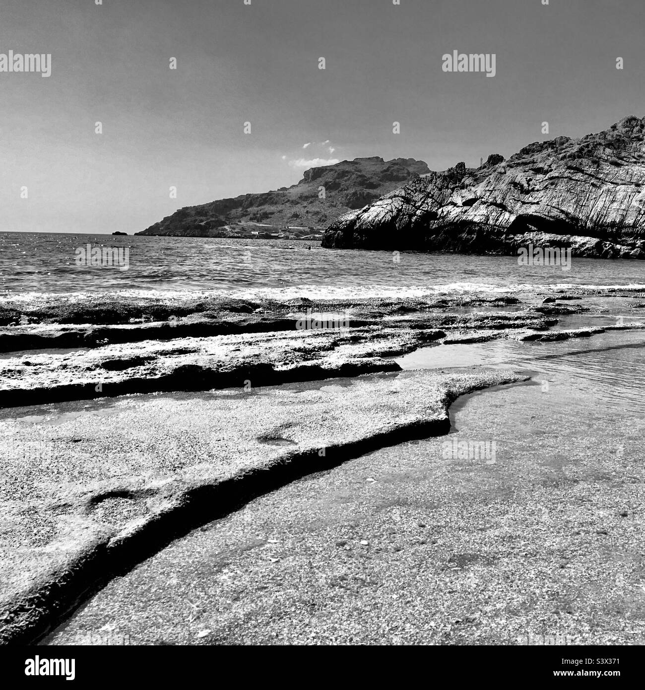 A dramatic rocky Greek beach in the midday sun. Shot in black and white ...