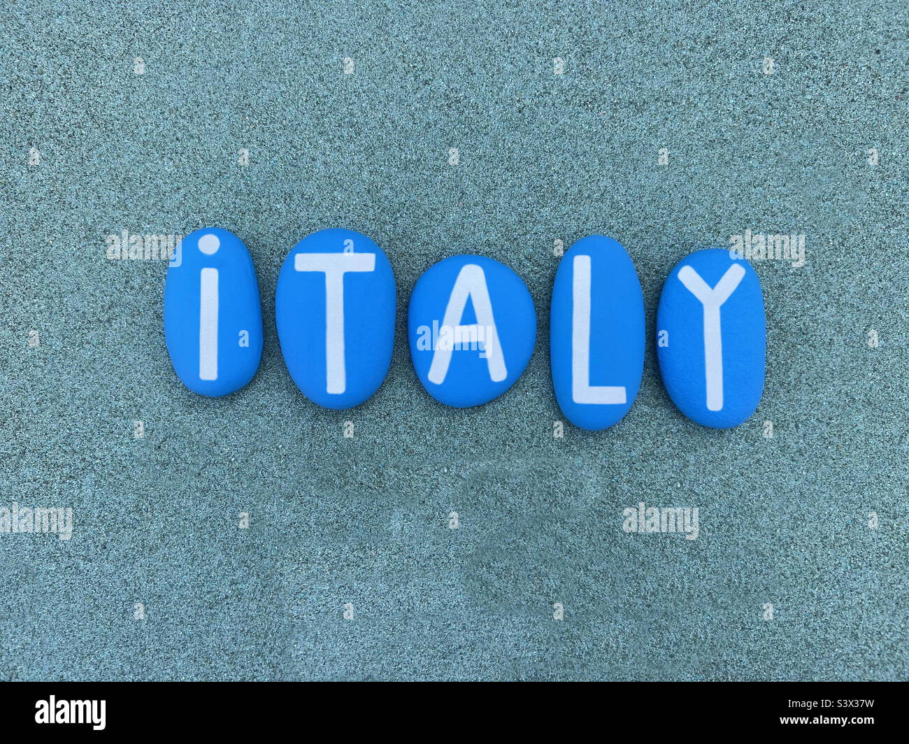 Italy, souvenir composed with blue colored stone letters over green sand - Smartphone Captured Stock Image