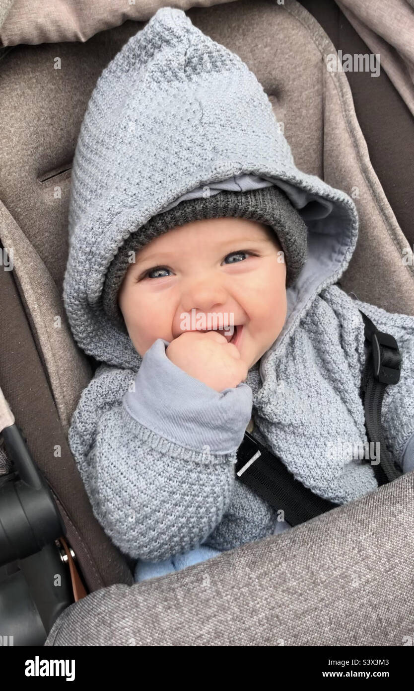 Smiling baby with fist in mouth sitting in pram with hood and hat Stock