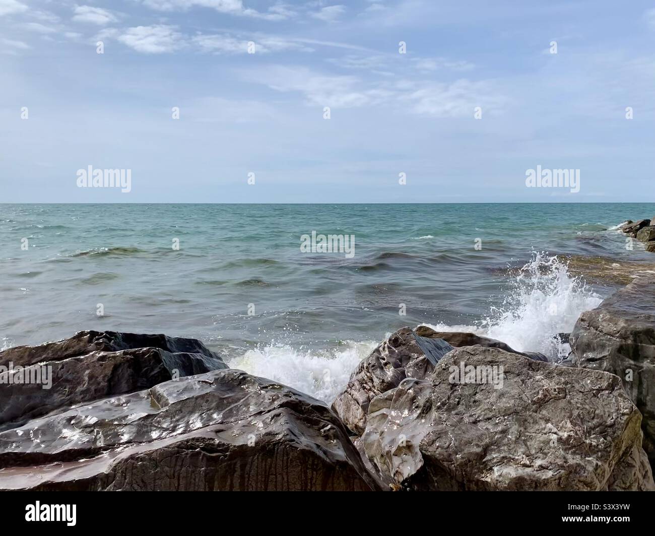 Waves crashing against wet shimmering rocks - Smartphone Captured Stock Image