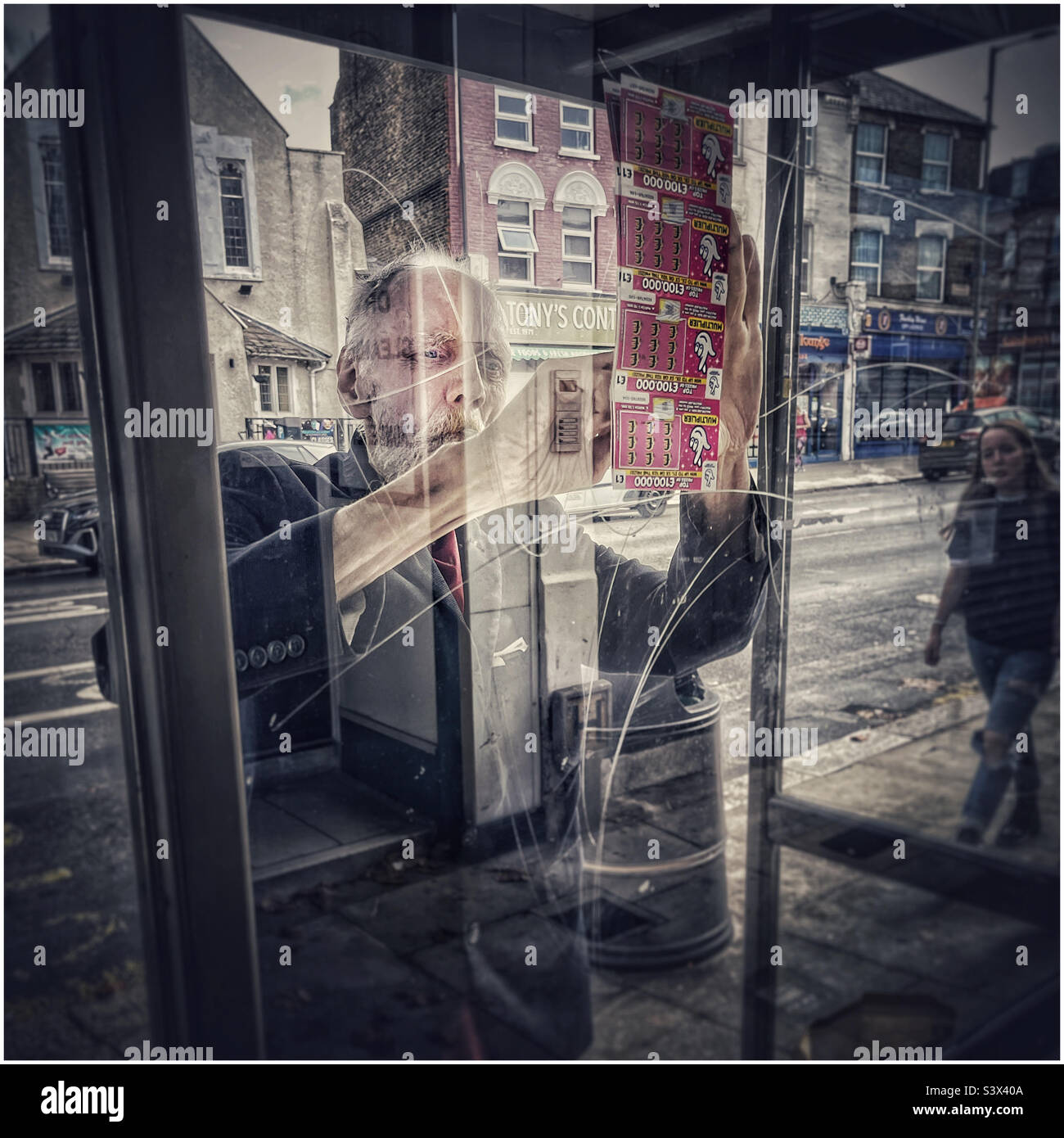 Elderly man with lottery scratch cards at a bus stop in East Finchley, North London - Smartphone Captured Stock Image