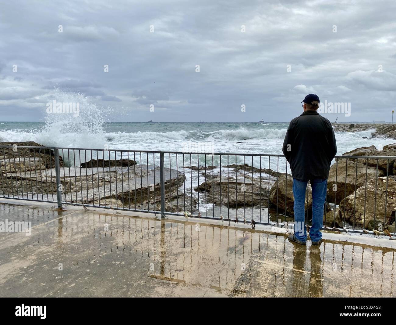 Man standing by railings on a rocky shore in winter Stock Photo
