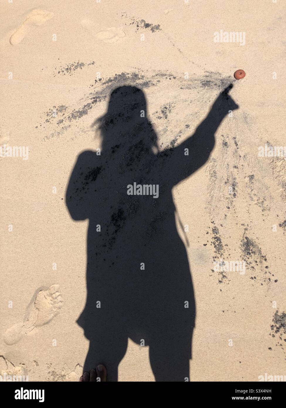 The shadow of a woman in sand pointing. Stock Photo