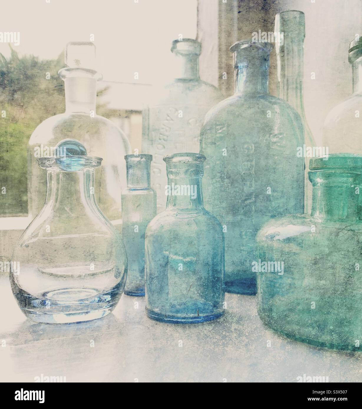 A collection of antique coloured glass bottles on a windowsill in daylight Stock Photo