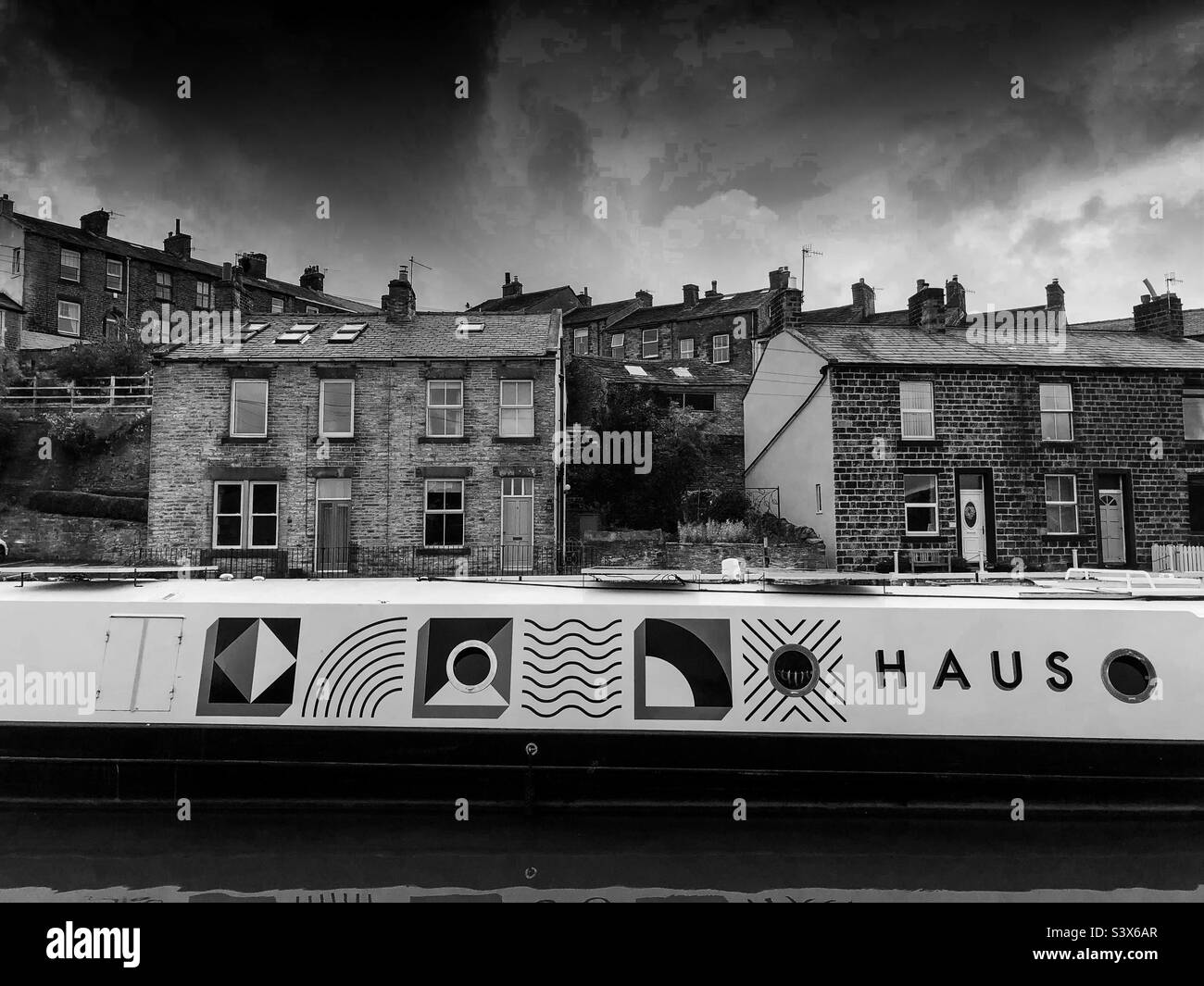 Haus at Kildwick on a canal boat with the back drop of stone built terraced houses. Stock Photo