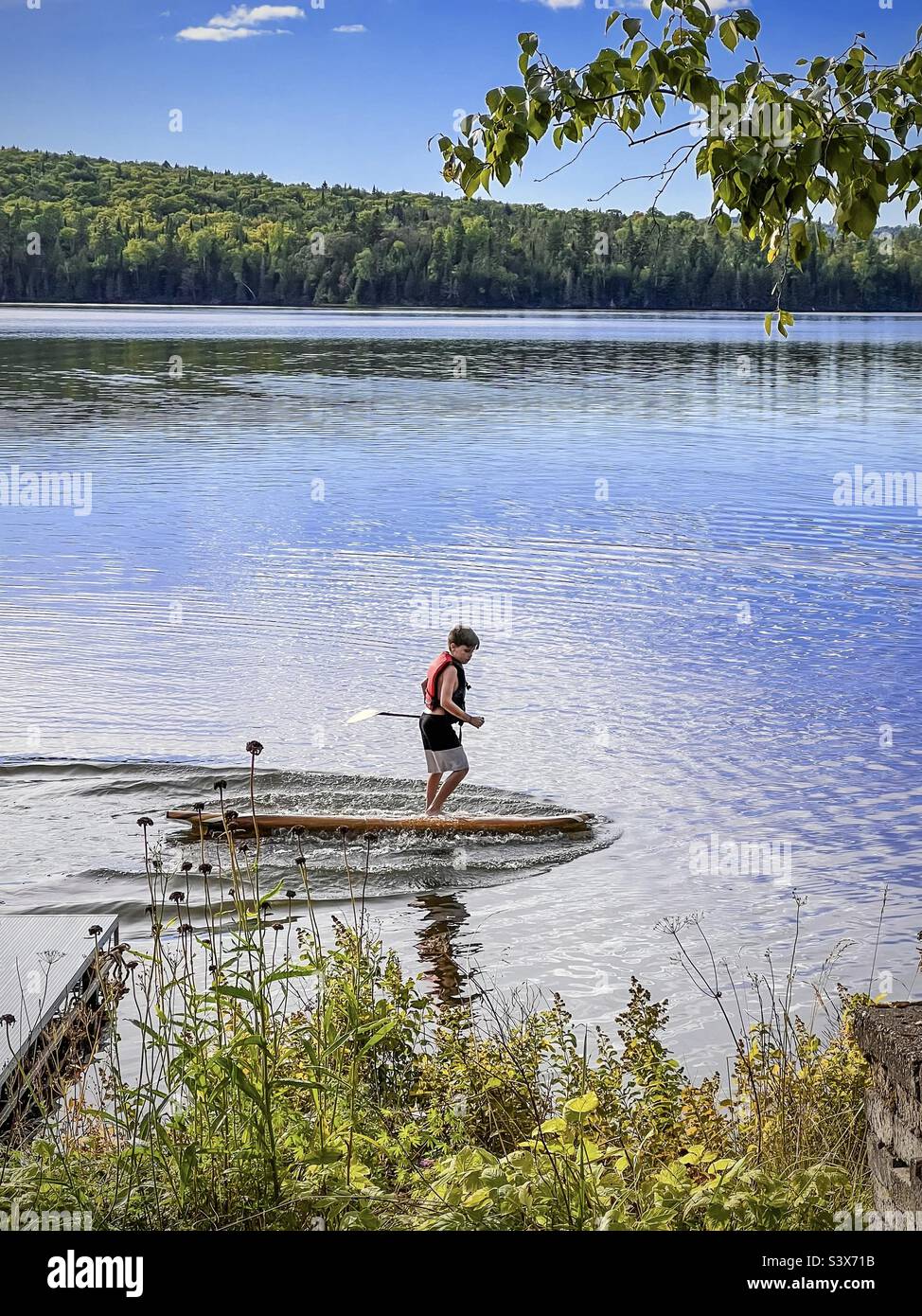 A 12 year old boy playing on a paddle board, splashing the water with it as he totters back and forth. - Smartphone Captured Stock Image
