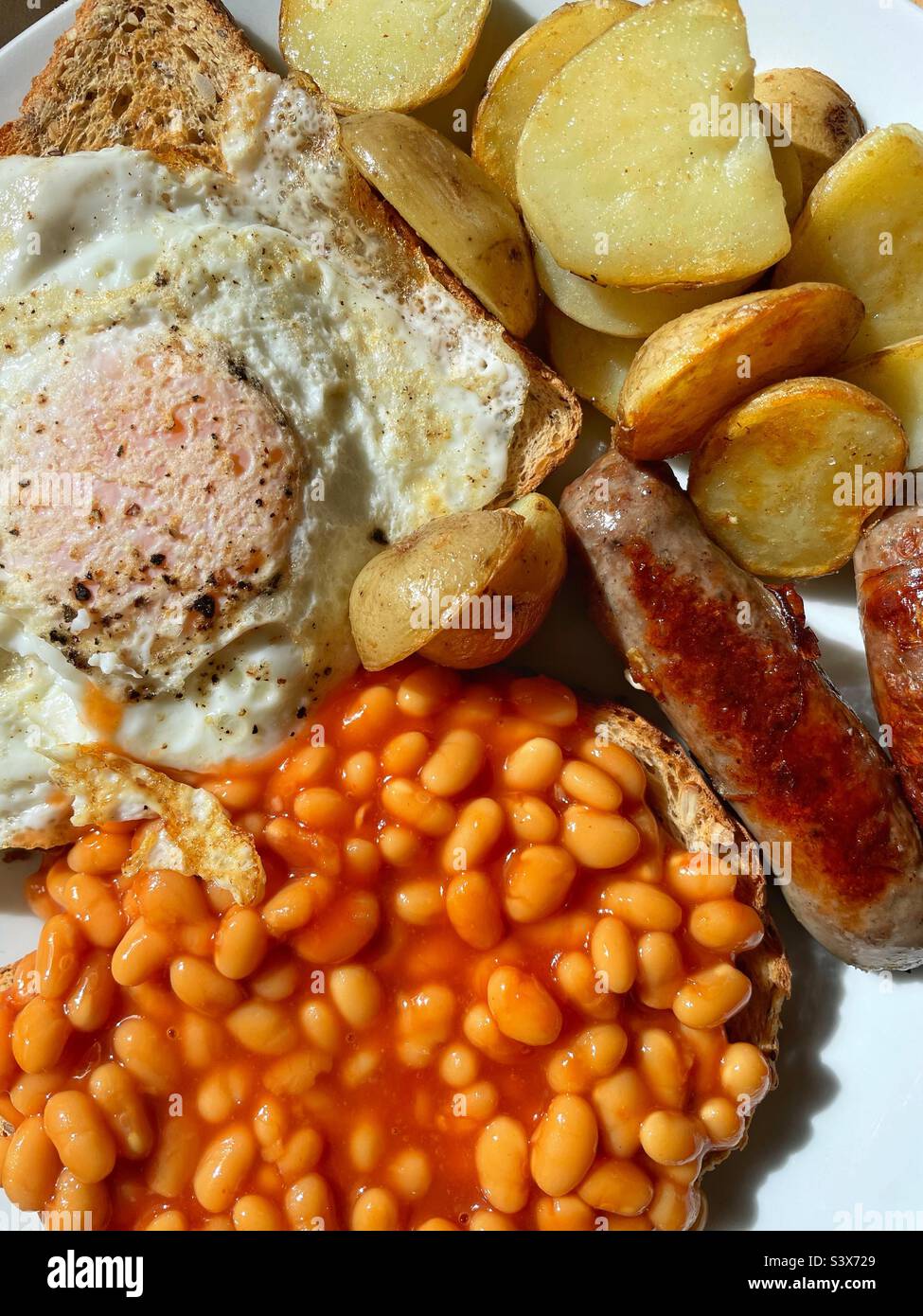 Brunch - fried potatoes, fried eggs, sausages and beans. Stock Photo
