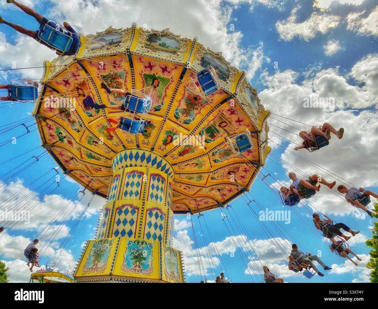 Happy people riding on a “chair o plane” or swing ride at a funfair. It’s summer holidays and time to relax and have fun! Photo ©️ COLIN HOSKINS. Stock Photo