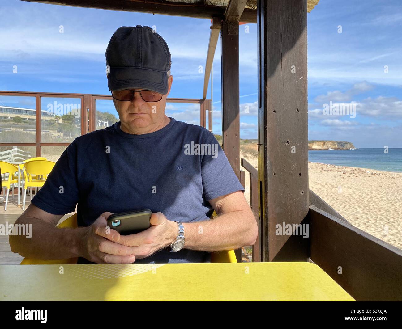 Remote working, man sitting in a beach cafe working on his mobile phone Stock Photo