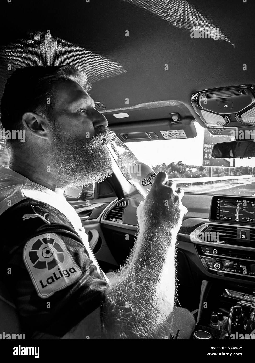 Hairy man drinking beer in car as a passenger while driving Stock Photo