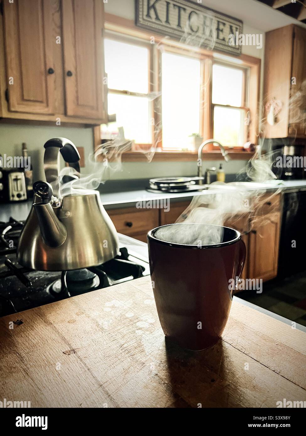 Steam rising from a teakettle on the stove and a mug on the butcher’s ...