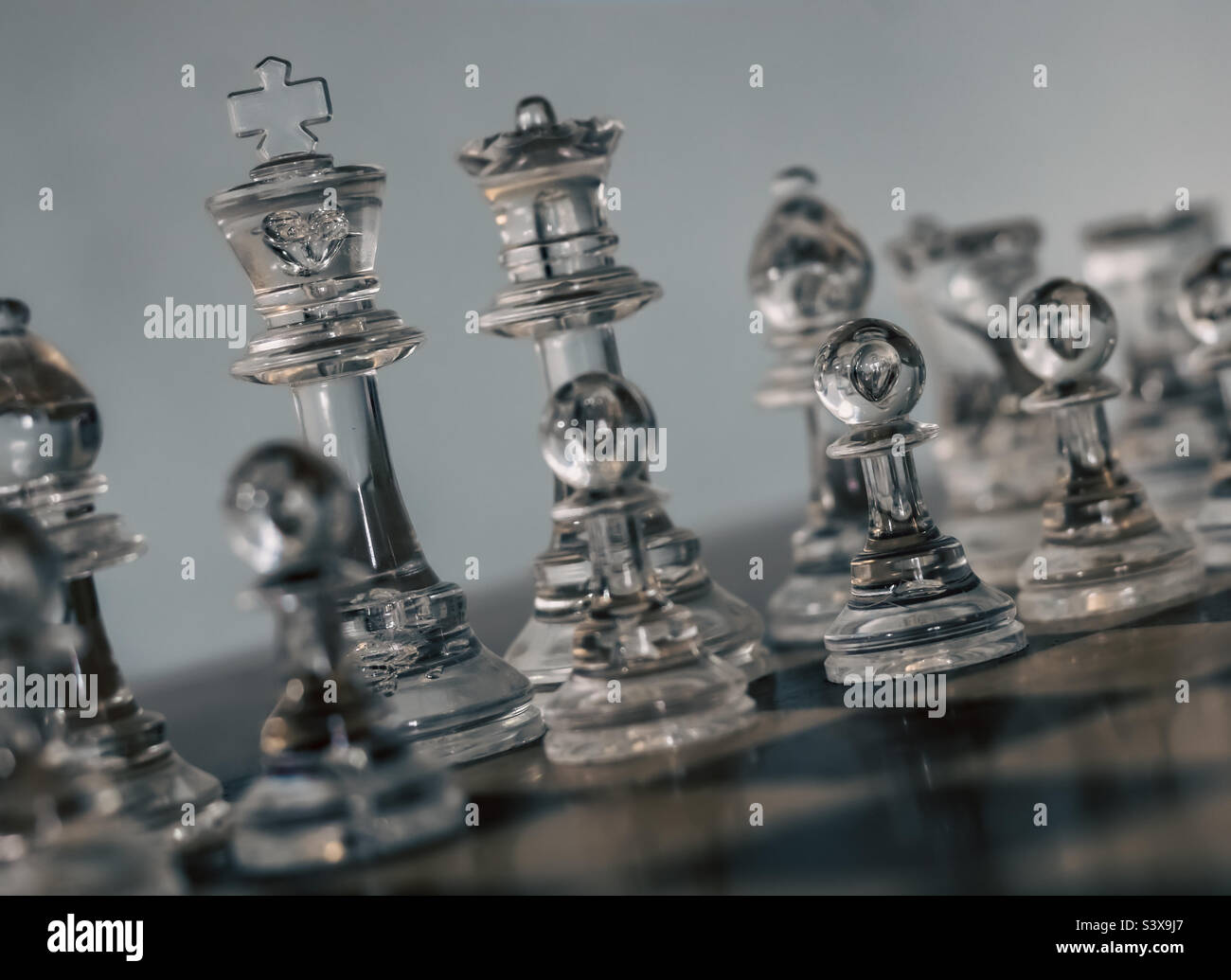 Clear chess pieces on a board at a diagonal angle, with focus on the king and a pawn - Smartphone Captured Stock Image