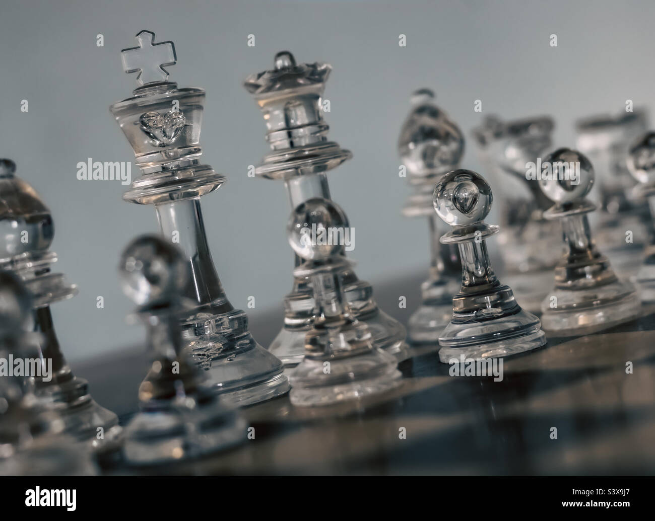Clear chess pieces on a board at a diagonal angle, with focus on the king and a pawn Stock Photo