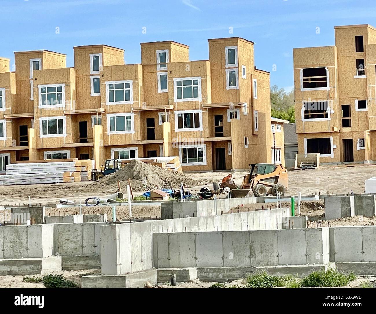 New housing going up at a Utah, USA construction site. Workers have left for the day but remnants of their work in progress can be seen, including heavy equipment and various materials and supplies. - Smartphone Captured Stock Image
