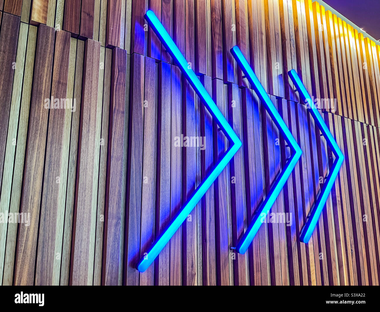 Blue neon chevron arrows on wooden clad wall Stock Photo