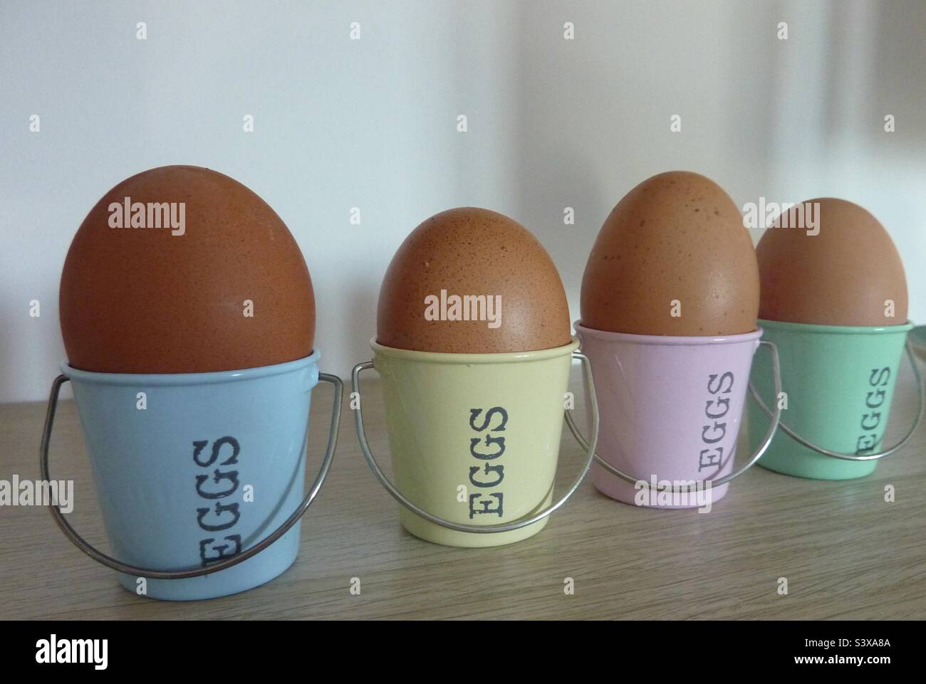 Eggs in Pastel Coloured Egg Cups (“Buckets”) On a Wooden Shelf Stock