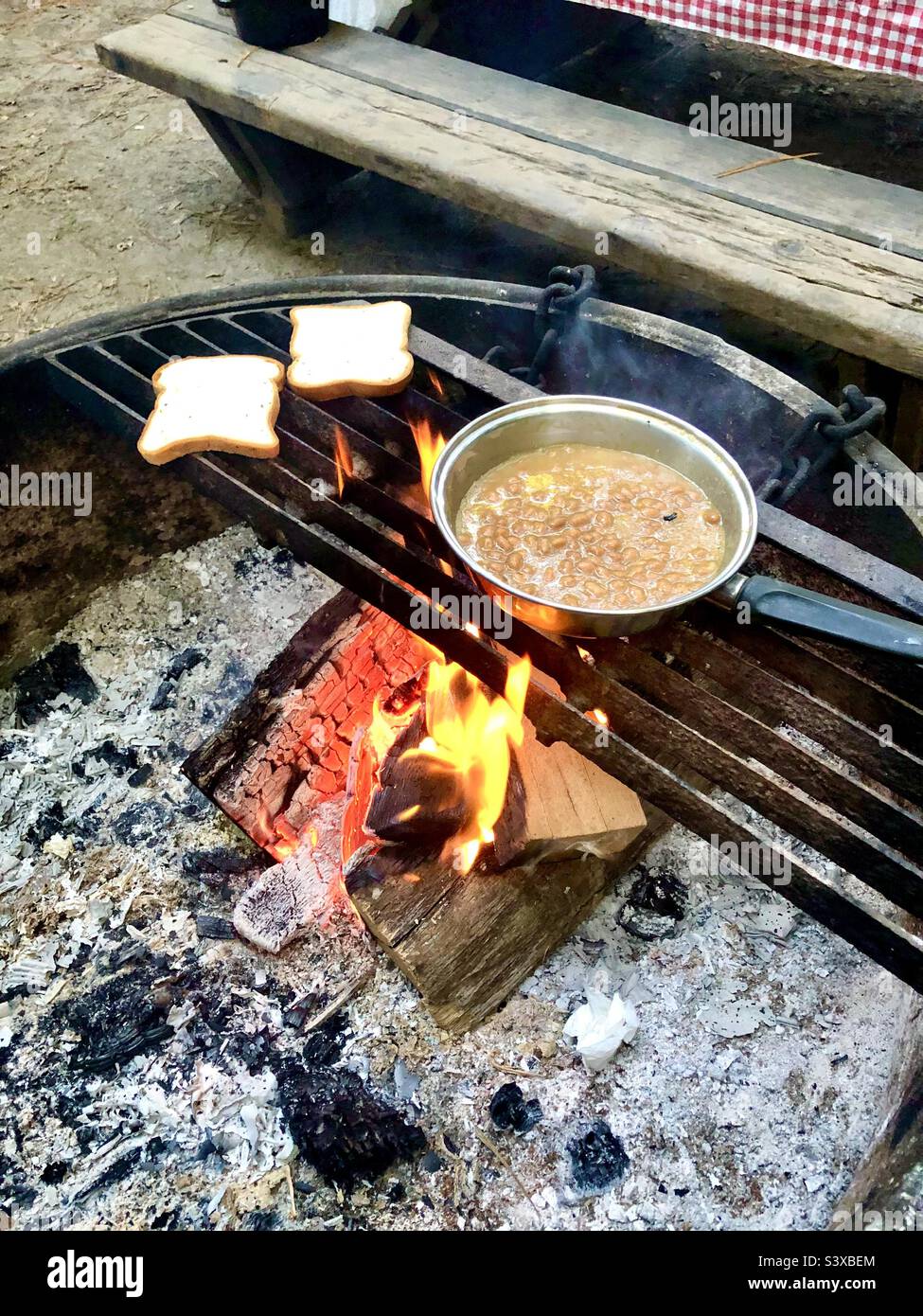Two slices of bread and a pan of beans cook over an open fire Stock