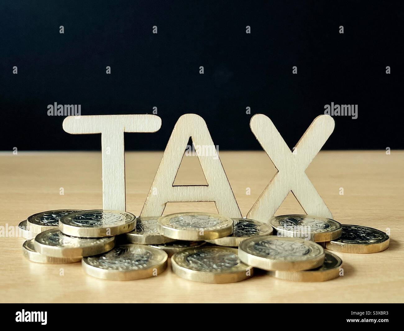 Tax in wooden letters surrounded by British one pound coins. Earnings and income concept. No people. Stock Photo
