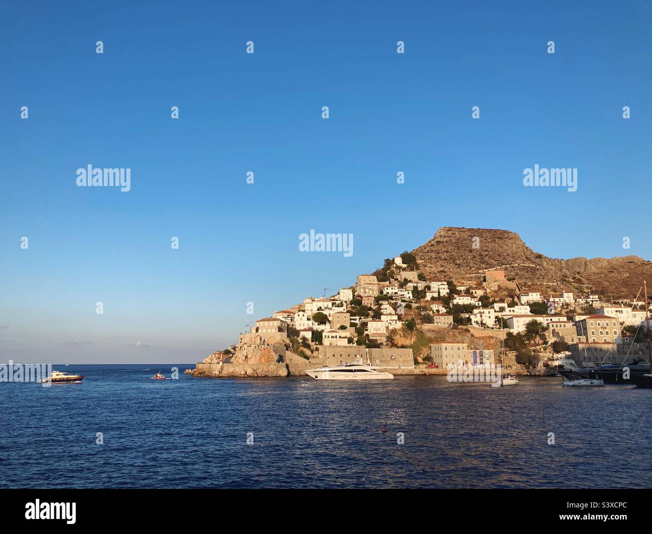 View of Hydra, Greece, as the sun sets and casts a golden light on the island - Smartphone Captured Stock Image