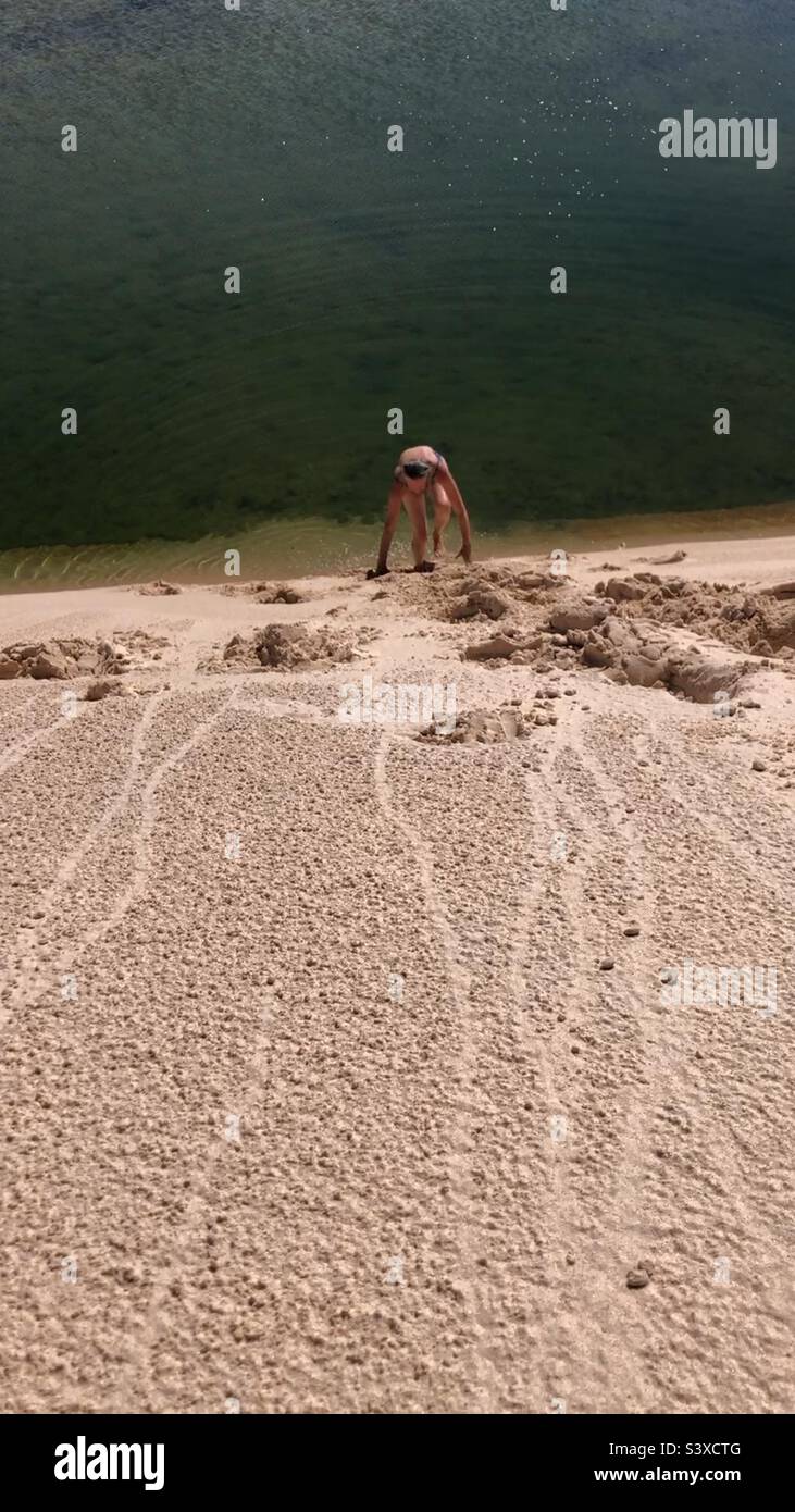 A woman climbing up a sand dune. Stock Photo