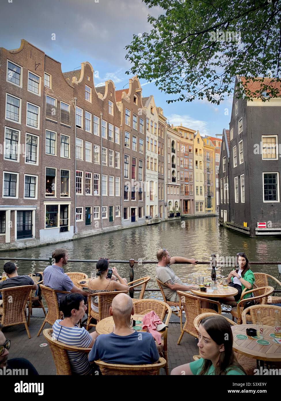 Canal life at a restaurant bar on a beautiful summer evening during golden hour in the heart of Amsterdam - Smartphone Captured Stock Image