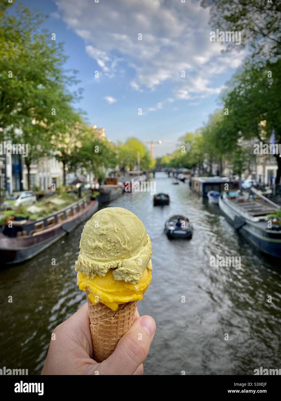 A tourist enjoys an ice cream on a beautiful summer evening on a bridge over the canals of Amsterdam - Smartphone Captured Stock Image