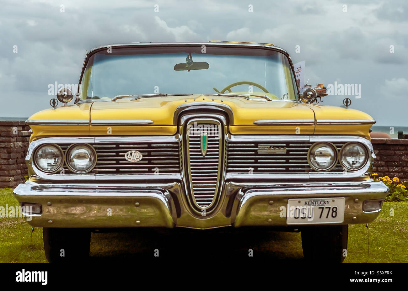 A bright yellow Haas 1950s convertible complete with diner tray on the side, against a blue and cloudy sky - Smartphone Captured Stock Image