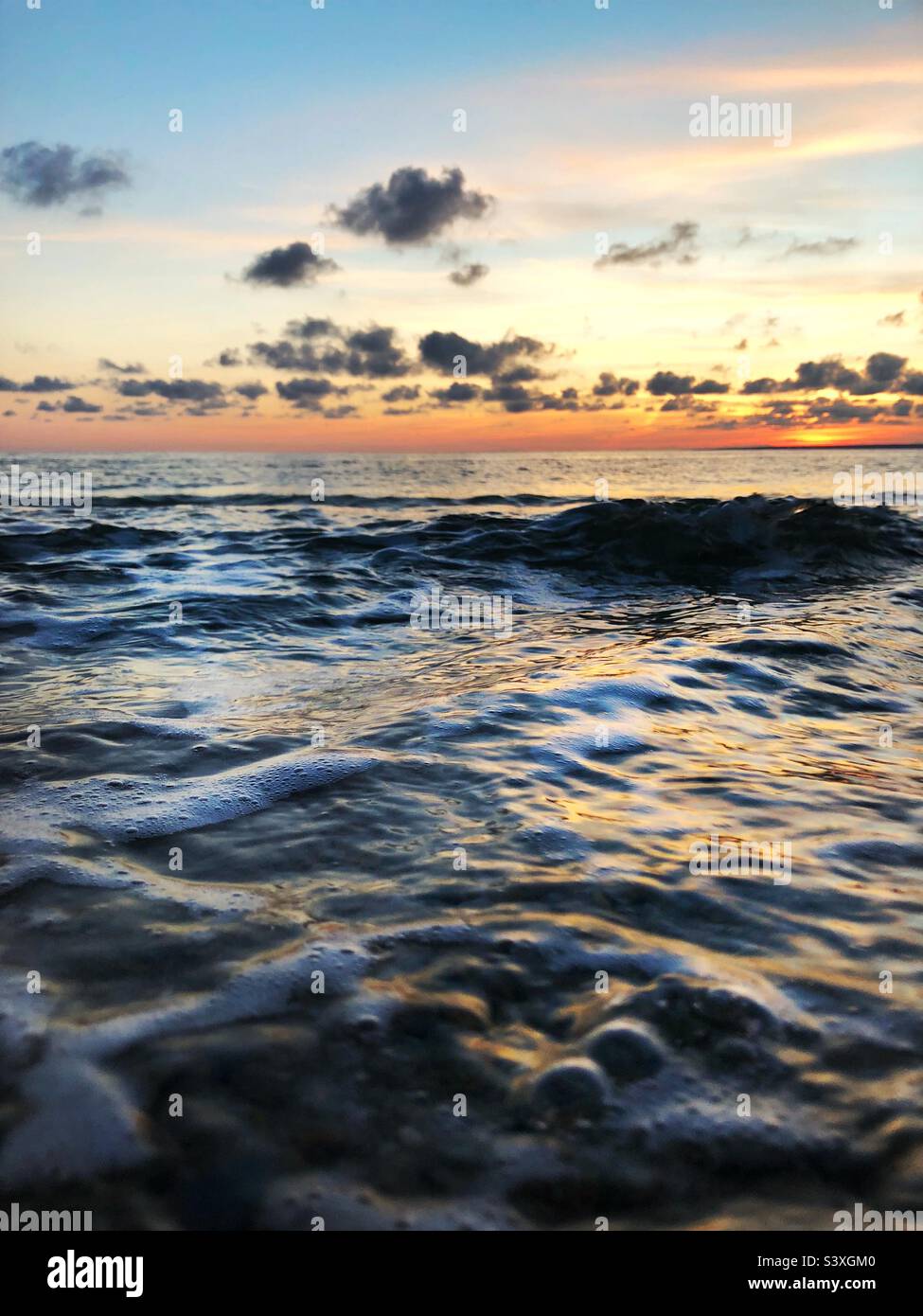 close up of waves and bumbling surf on the surface of a sunlit ocean during the golden hour at sunset with copy space - Smartphone Captured Stock Image