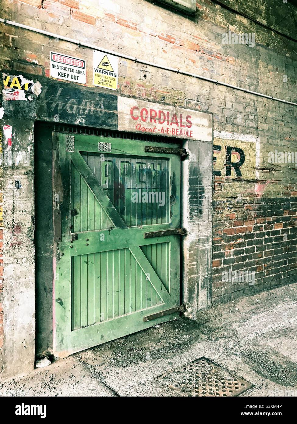 Green rustic door in a dark alleyway with red brick and vintage sign-writing, in central Invercargill, New Zealand. Stock Photo