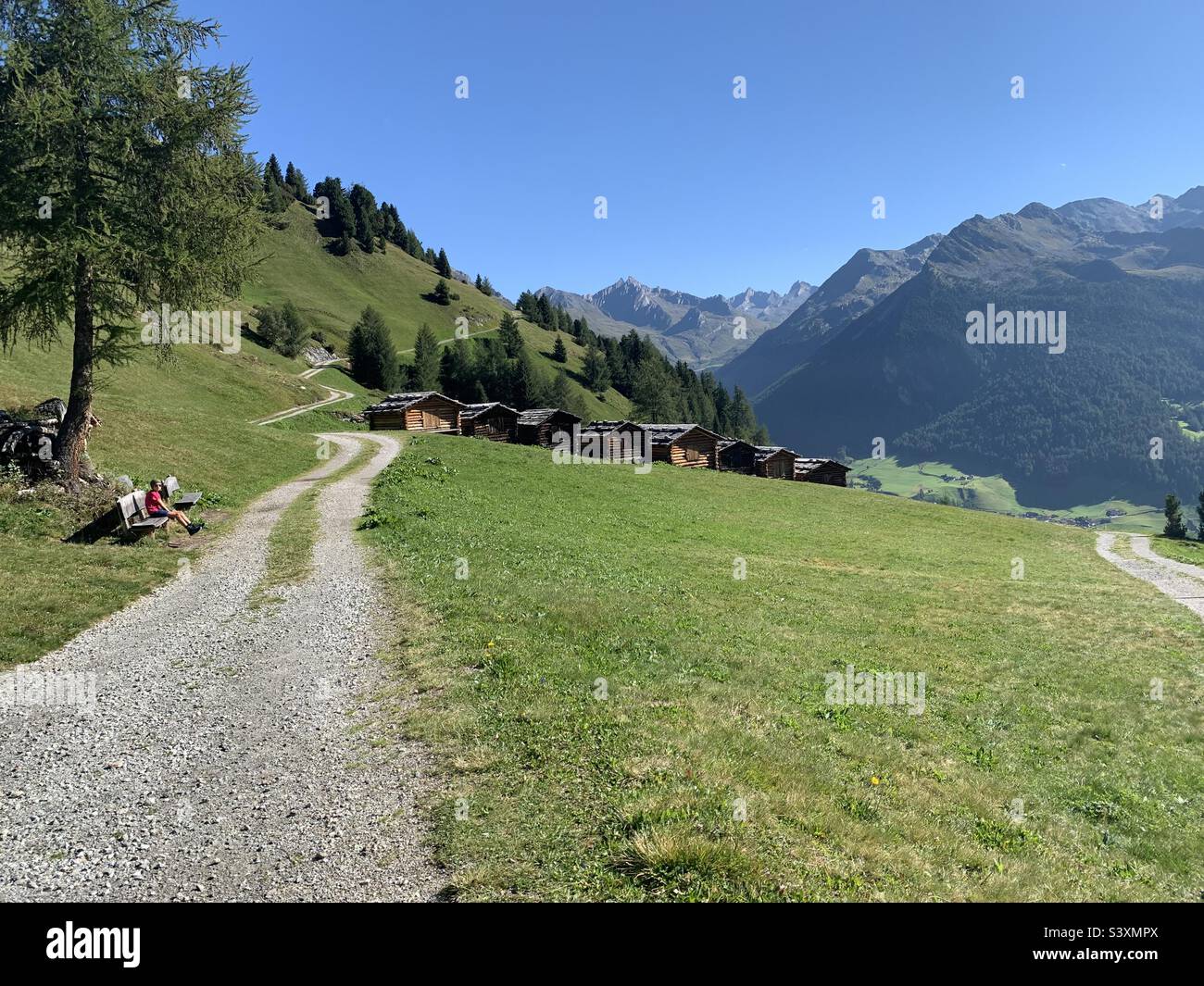 Barns and girl sitting on a bench in mountain scenery. - Smartphone Captured Stock Image