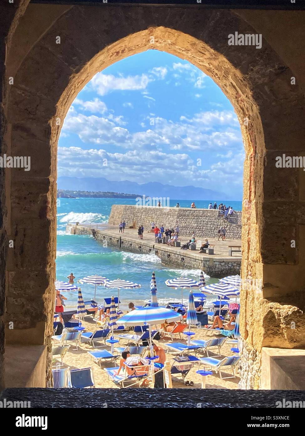 View through the city wall gateway in Cefalu Sicily - looking through to the beach and harbour wall - Smartphone Captured Stock Image