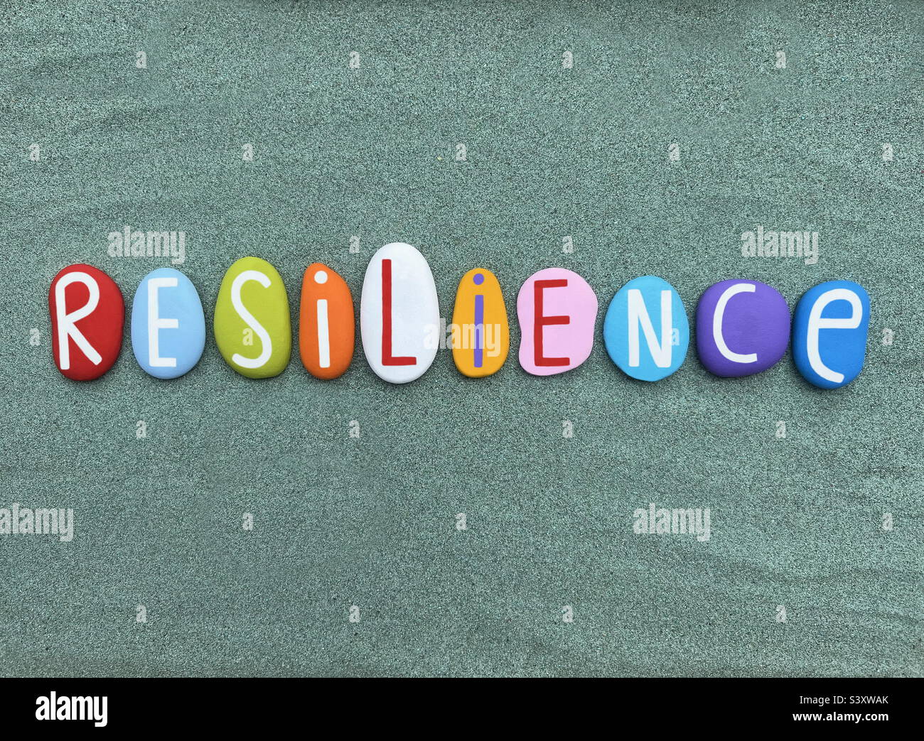 Resilience word composed with hand painted stone letters over green sand - Smartphone Captured Stock Image