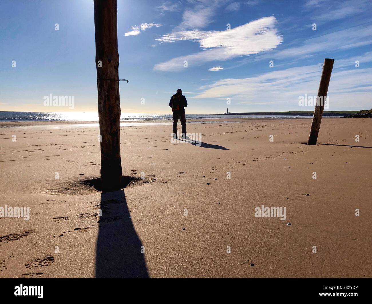 Backlit man standing on a beach at low tide - Smartphone Captured Stock Image
