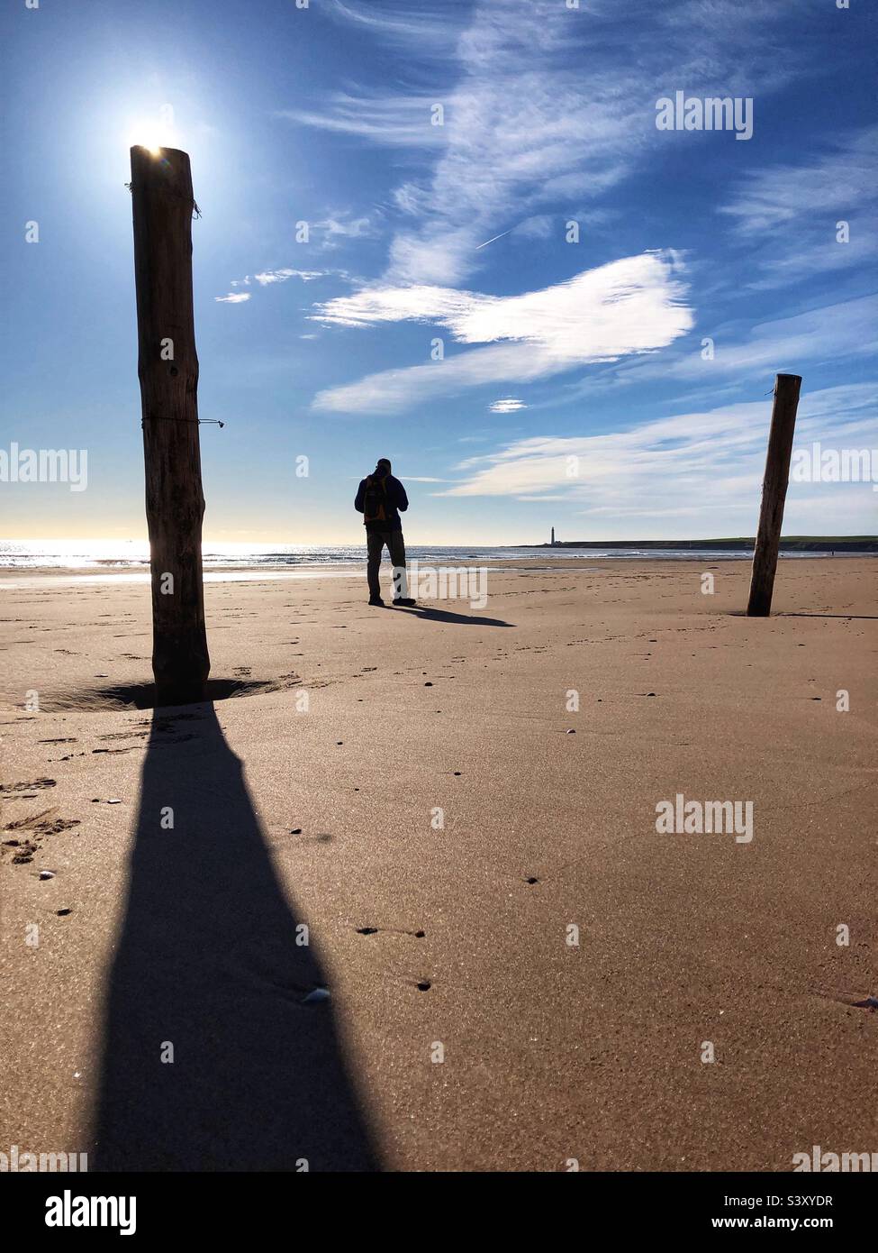 Backlit man standing on a beach at low tide - Smartphone Captured Stock Image