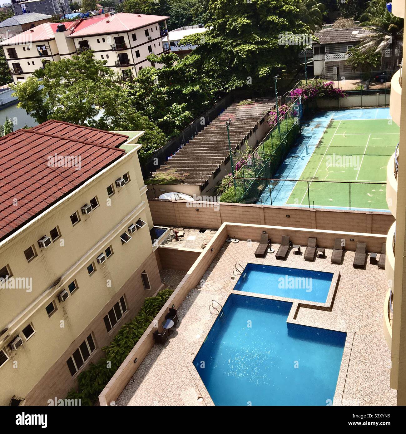 A very good looking view of buildings and it’s environ with pool,a tennis court,trees and greens Stock Photo