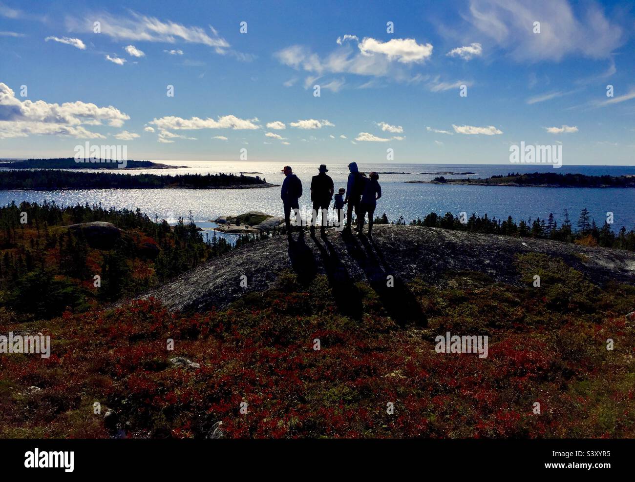 Family outdoors: nature, rocks, and the ocean on a blue sky day, Nova Scotia, Canada. People silhouetted. - Smartphone Captured Stock Image
