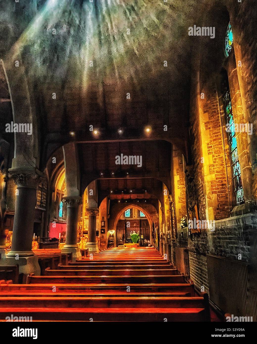 Looking down the pews towards a side Chapel where a priest has hands outstretched. Holy Trinity Church, Folkestone, Kent is a Grade II Listed building architecturally important. - Smartphone Captured Stock Image
