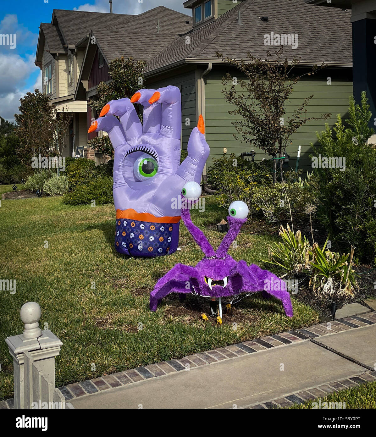 Scary spooky fuzzy big purple spider with fangs and googly eyes and huge hand with single green eye in center and long orange fingernails Halloween yard decorations Stock Photo