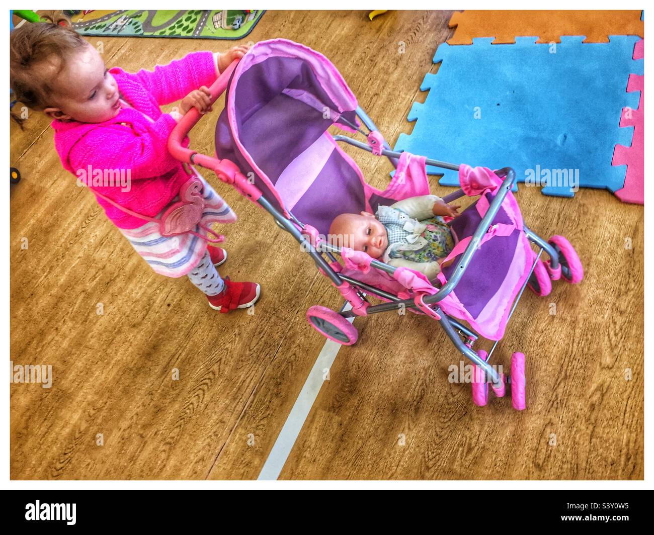 Toddler girl pushing a toy pram at a playgroup - Smartphone Captured Stock Image