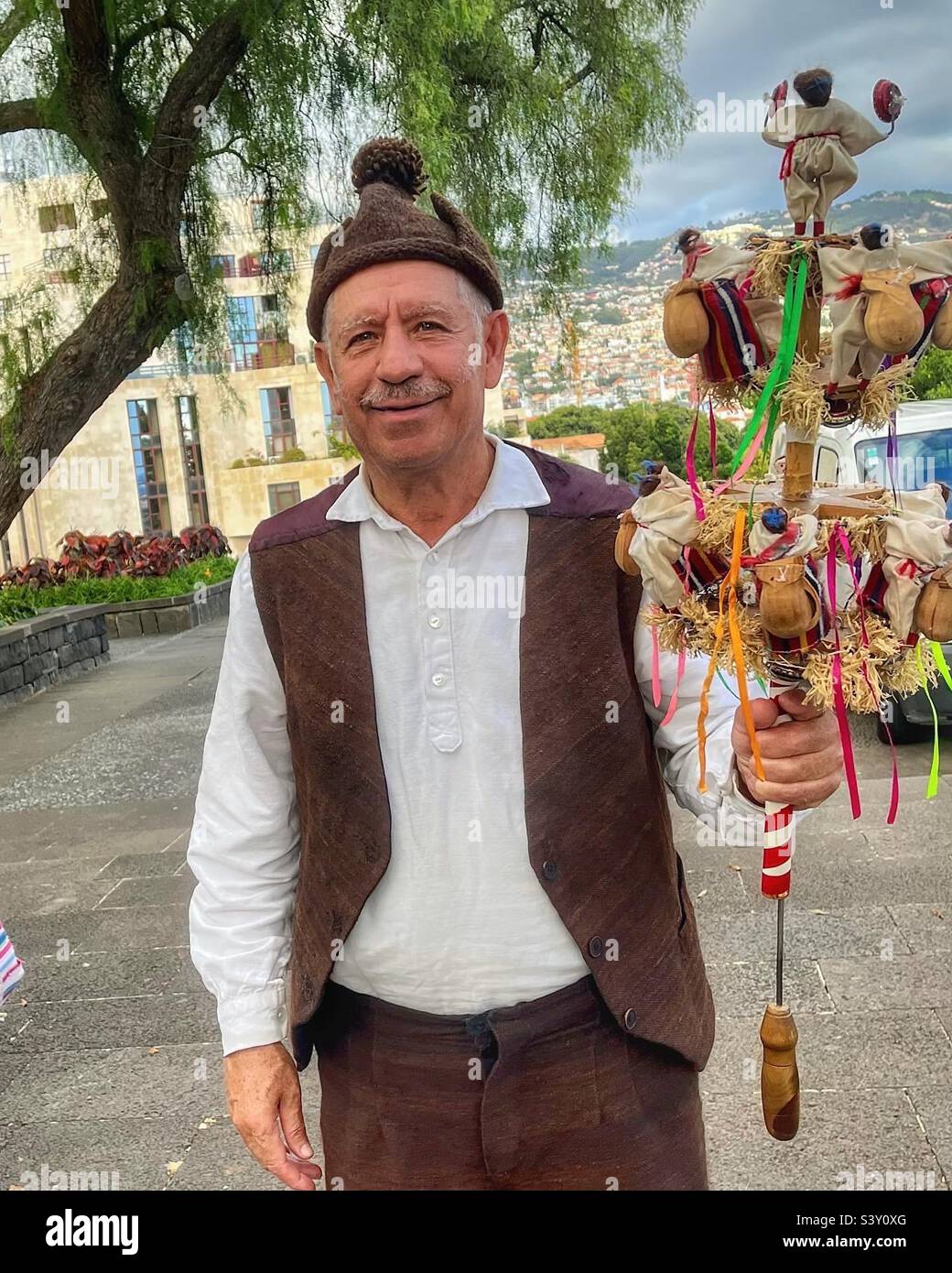 Man in traditional dress of Madeira, Portugal holds a Brinquinho - a set of wooden dolls with castanets affixed to a reed that is moved vertically to make the sounds. Pictured in Funchal. - Smartphone Captured Stock Image