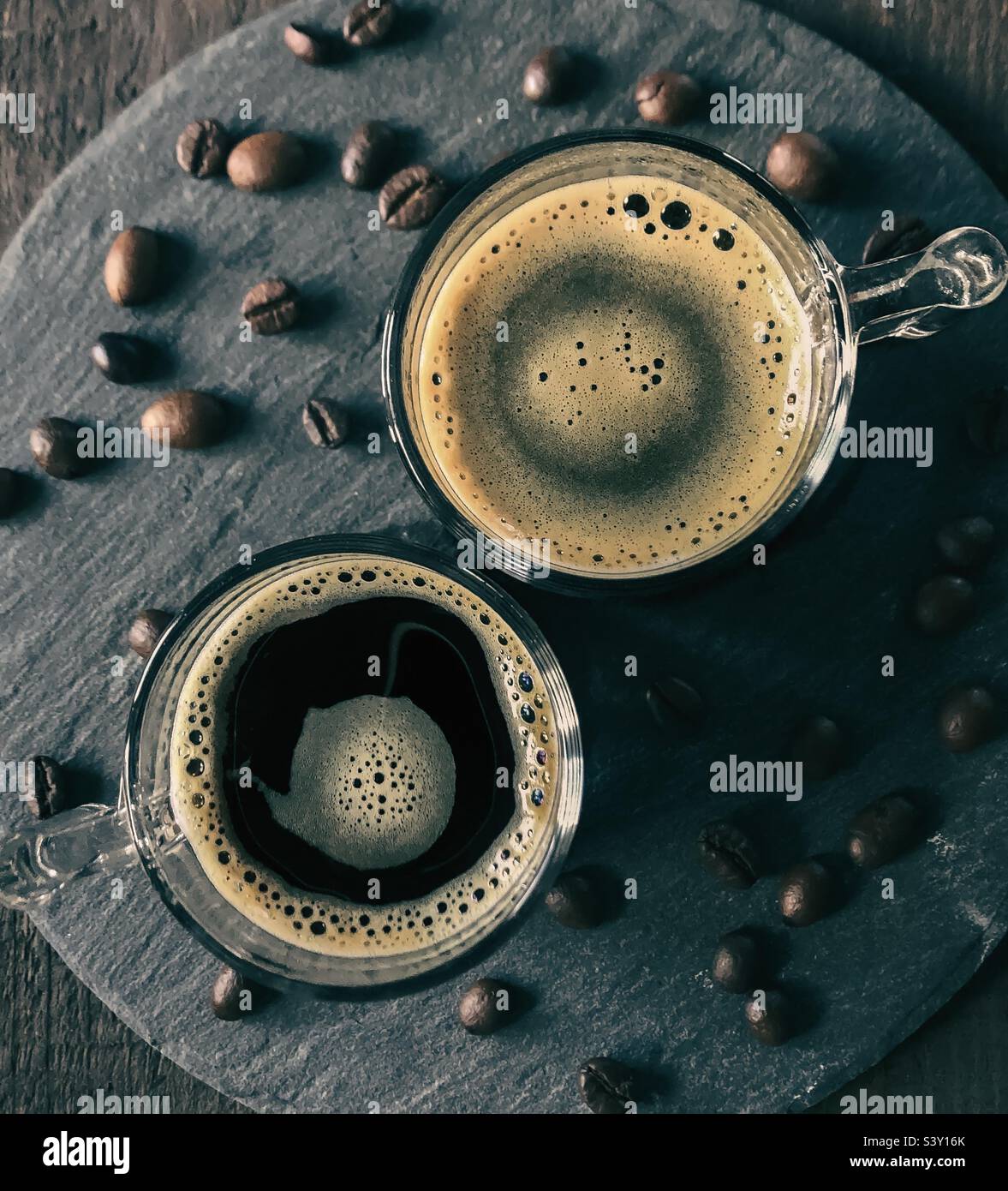 2 glasses of black, frothy coffee, viewed from above on slate with coffee beans - Smartphone Captured Stock Image