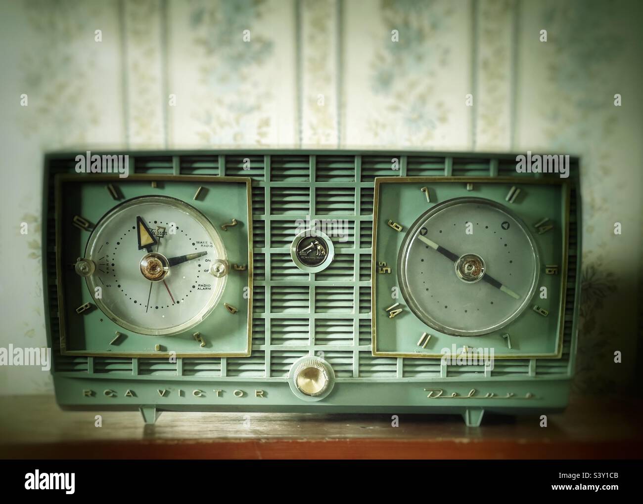 Pale green vintage RCA Victor clock radio on a wooden shelf with vintage floral wallpaper in background Stock Photo