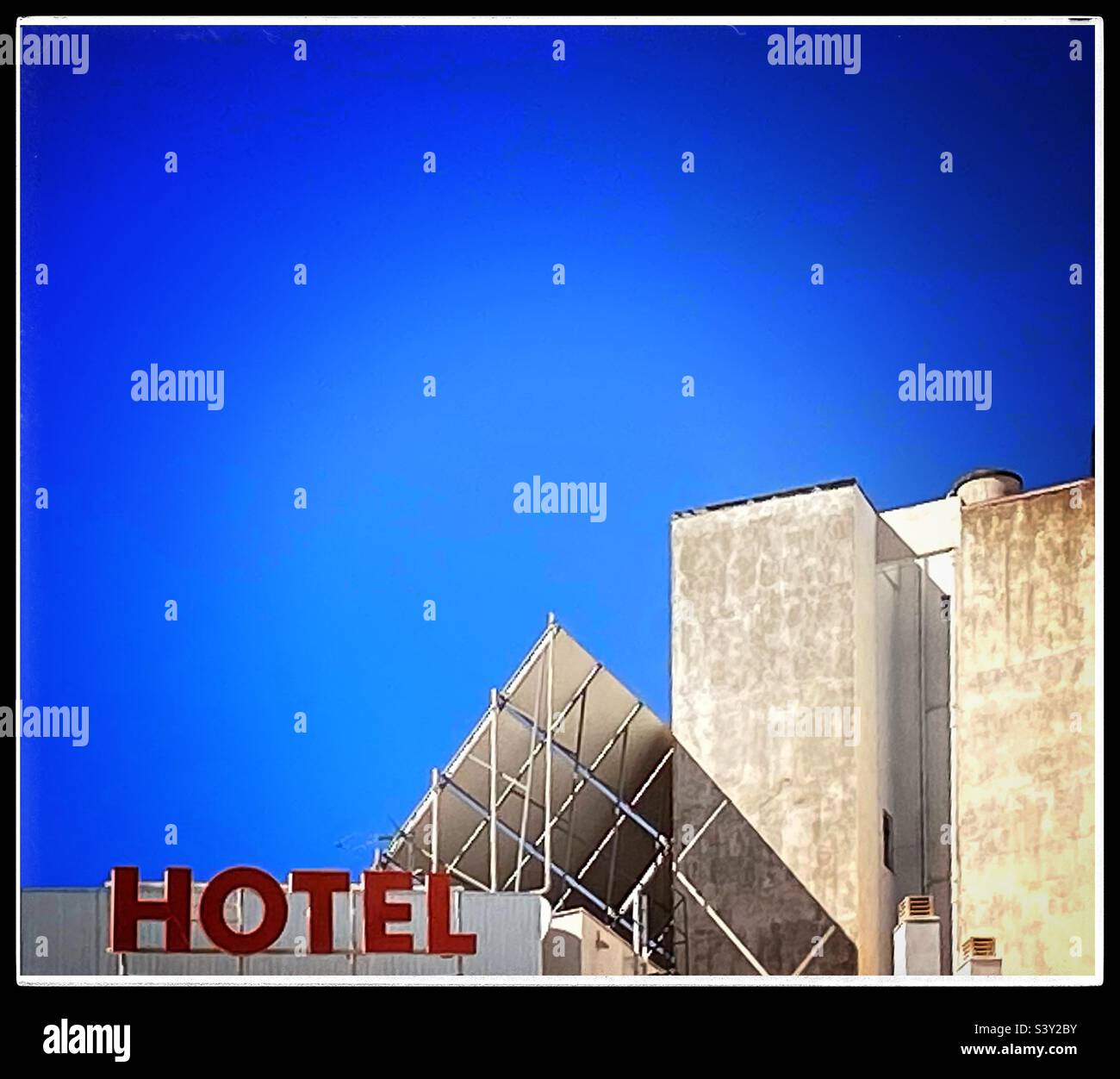 The signage of a hotel is displayed in bold red letters on the rooftop set against a cloudless blue sky. An array of solar panels capture energy from the sun. - Smartphone Captured Stock Image