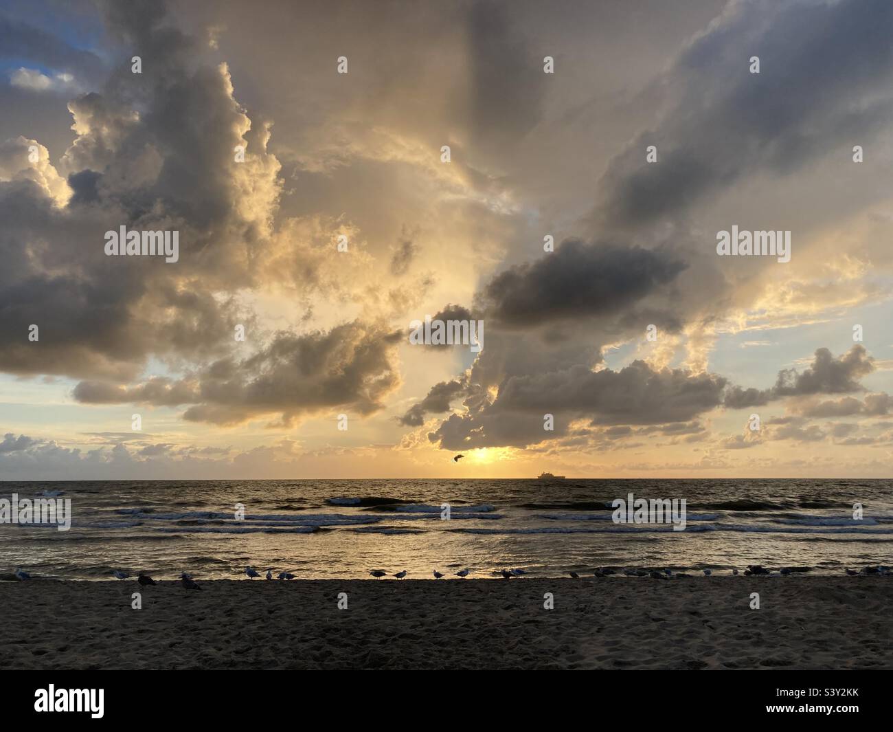 at the sea the red-golden sun shines out from behind the clouds before it sets - Smartphone Captured Stock Image