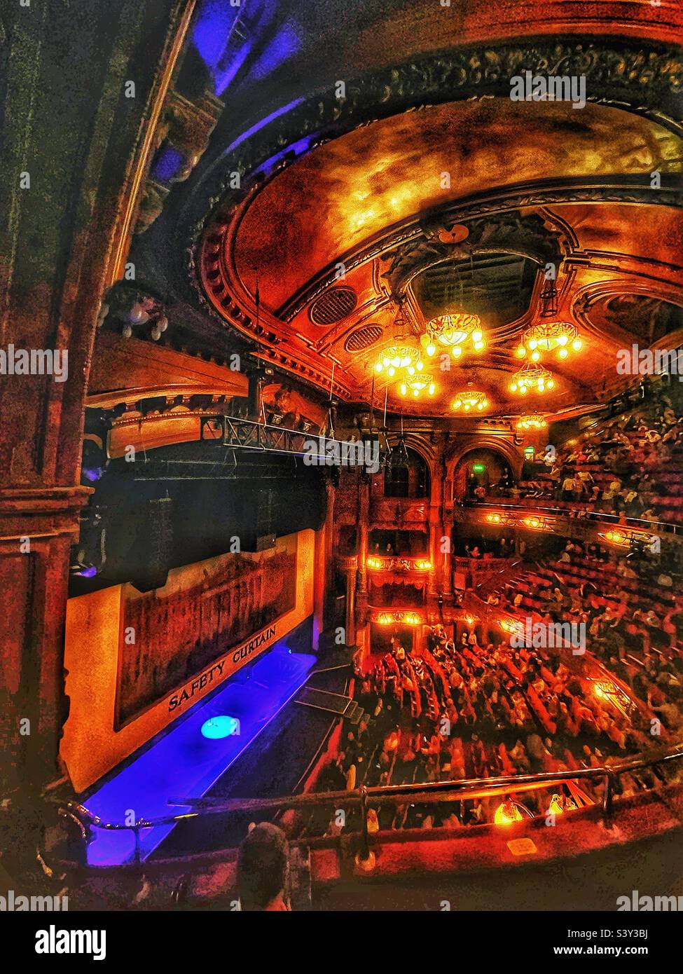 The spotlight appears as the safety curtain rises at London Palladium an historic theatre in Soho. The famous Royal Box is occupied by two gentlemen and the audience awaits the stage show start. - Smartphone Captured Stock Image