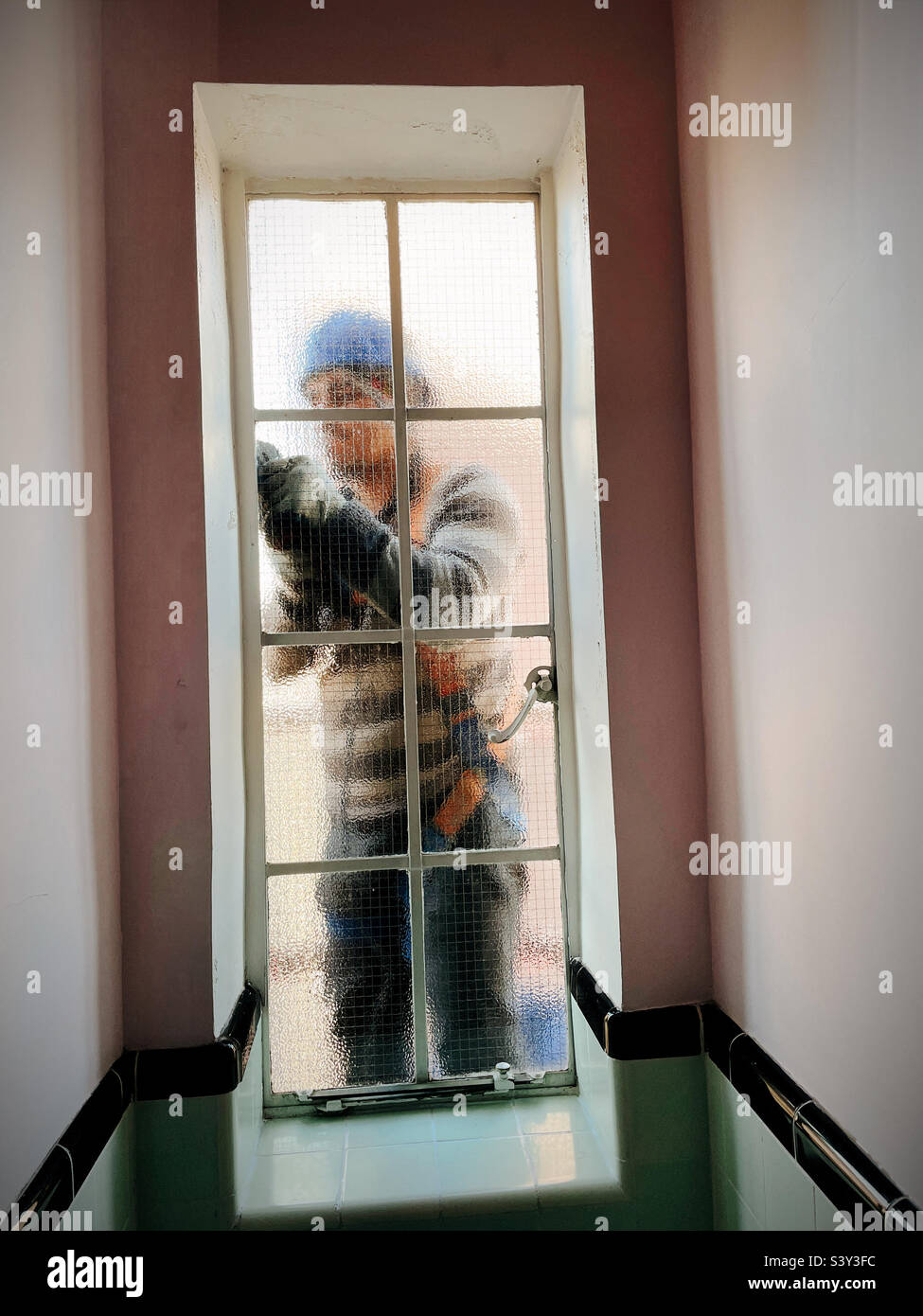 Construction worker on a suspended platform working on the outside of a casement window on a high-rise apartment building in Murray Hill, 2022, New York City, USA - Smartphone Captured Stock Image