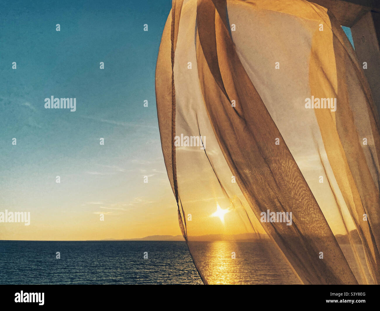 Sunset over Lardos Bay from Pefkos on Rhodes viewed through fluttering curtain Stock Photo
