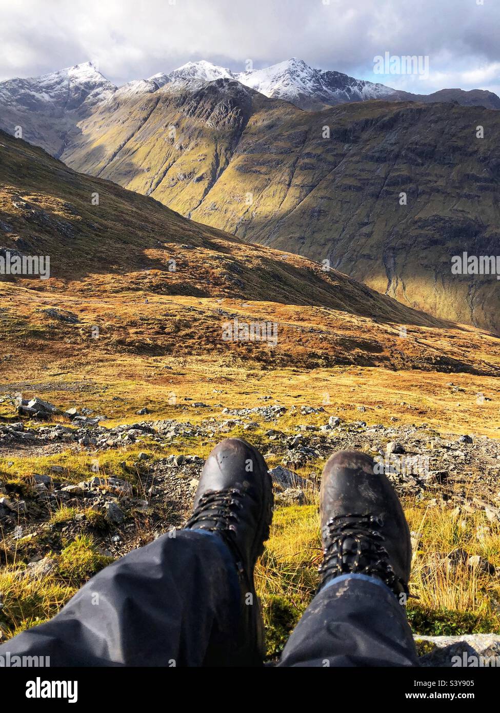 View of Walkers feet and leather boots on the path and slopes of Munro Buachaille Etive Beag, with a view of snow capped peaks of Bidean nam Bian, Glencoe, Scotland - Smartphone Captured Stock Image