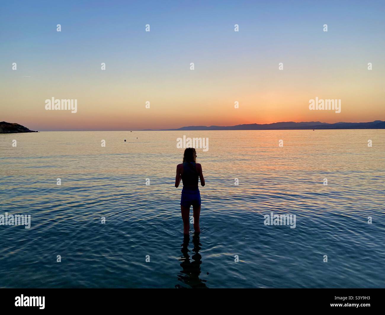 Girl in silhouette paddling in Lardos Bay at sunset. Pefkos on island of Rhodes, Greece Stock Photo